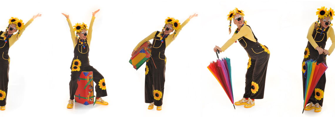 Clownin mit Sonnenblumen auf dem Kopf und auf der Kleidung trägt einen Koffer und einen bunten Schirm